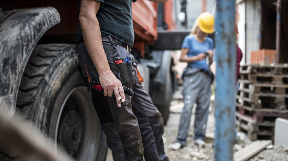 Worker leaning against commercial vehicle tire holding a cigarette while smoking in the workplace