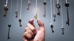 hand reaching for gold key among other keys hanging on strings