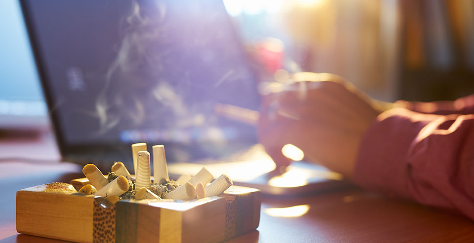 man smoking at a desk with ashtray full of smoked cigarettes in an office without a smoke-free policy