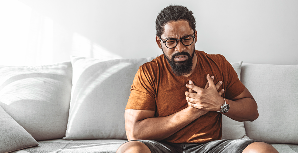 Man sitting on couch clutching chest because of heart disease and smoking