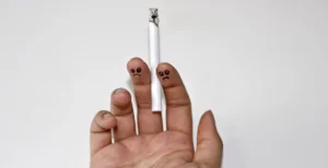 Hand holding a low nicotine cigarette with frowning faces drawn on 2 fingers to show the negative impacts of smoking.